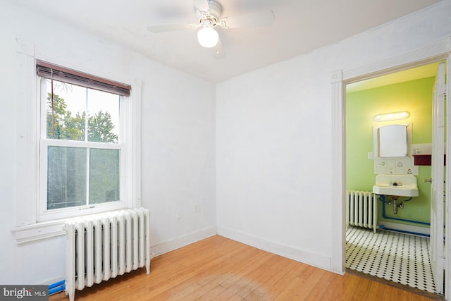 empty room with radiator, light hardwood / wood-style floors, and ceiling fan