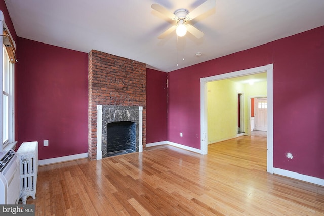 unfurnished living room with light wood-type flooring, a fireplace, ceiling fan, and a wealth of natural light