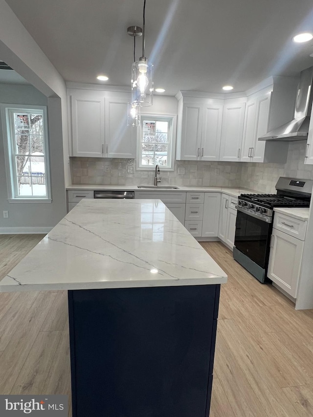 kitchen with wall chimney exhaust hood, light wood-style floors, stainless steel gas stove, and a sink