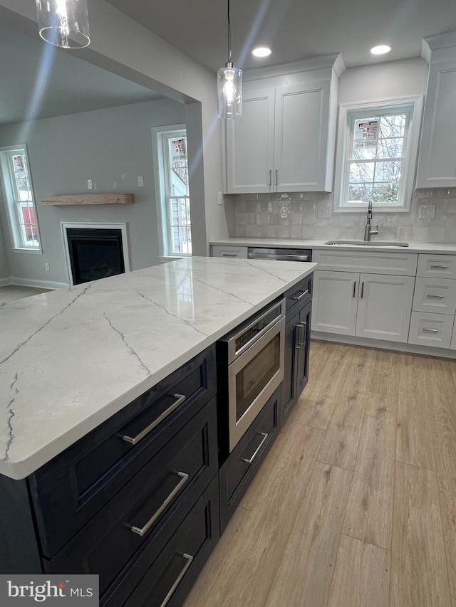 kitchen featuring a sink, stainless steel microwave, white cabinets, and light wood finished floors