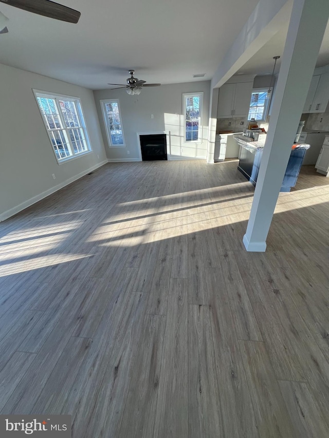 unfurnished living room with dark wood-type flooring, a fireplace, baseboards, and ceiling fan