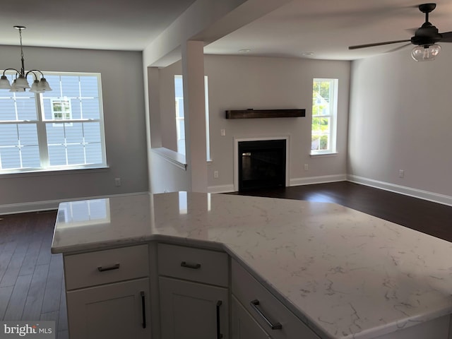 kitchen with light stone counters, a glass covered fireplace, dark wood-style floors, open floor plan, and white cabinetry