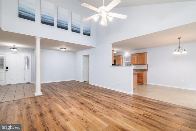 unfurnished living room featuring ceiling fan with notable chandelier, a towering ceiling, decorative columns, and light tile patterned flooring