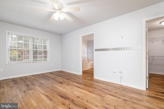 unfurnished bedroom with a walk in closet, a closet, light hardwood / wood-style flooring, and ceiling fan