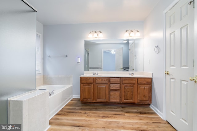 full bathroom with double vanity, wood finished floors, a garden tub, and a sink