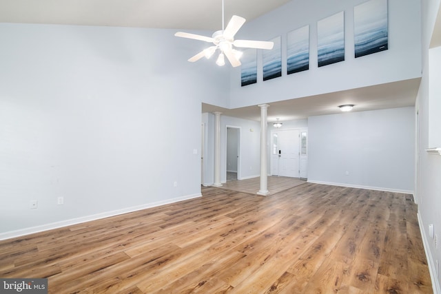 interior space with wood finished floors, a towering ceiling, decorative columns, baseboards, and ceiling fan