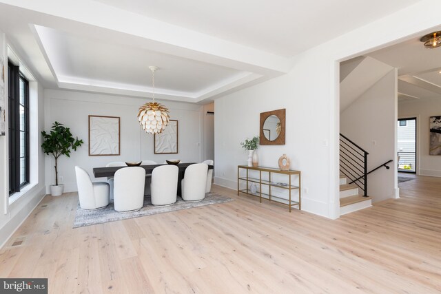 dining space featuring light wood-type flooring, a raised ceiling, an inviting chandelier, and a healthy amount of sunlight