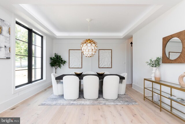 dining area featuring a raised ceiling, an inviting chandelier, and light hardwood / wood-style flooring