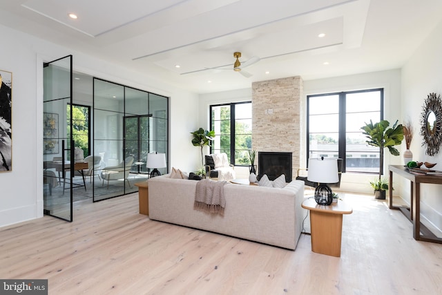 living room featuring light wood-type flooring, ceiling fan, a fireplace, and a raised ceiling