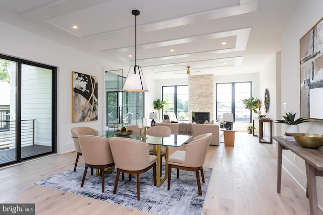 dining room featuring ceiling fan, light wood-type flooring, a tray ceiling, and a fireplace