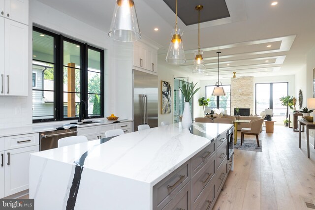 kitchen with built in appliances, a tray ceiling, hanging light fixtures, light wood-type flooring, and white cabinets