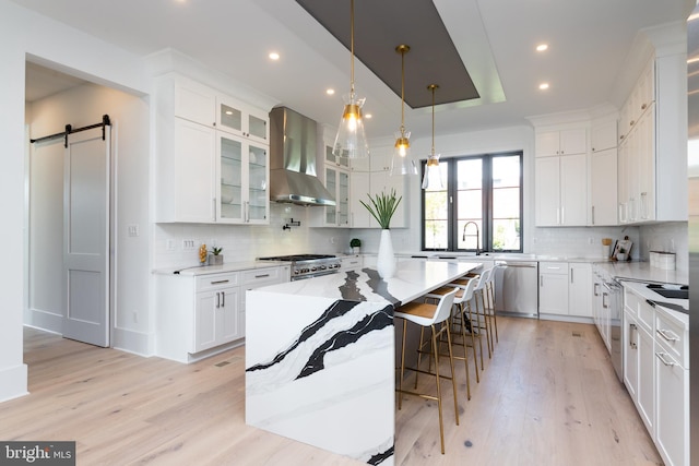 kitchen featuring a center island, stainless steel appliances, a barn door, wall chimney range hood, and white cabinets