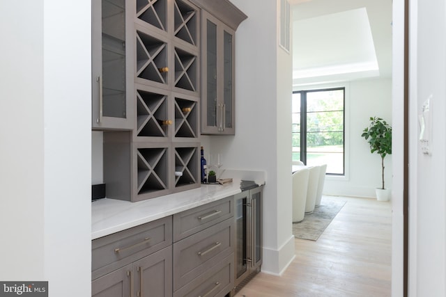 bar with wine cooler, light stone countertops, and light hardwood / wood-style floors