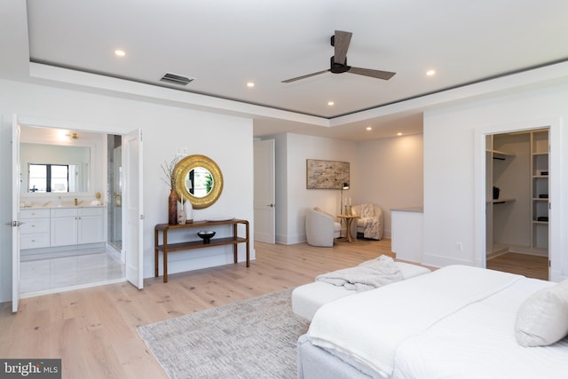 bedroom featuring light hardwood / wood-style flooring, ensuite bath, a tray ceiling, and ceiling fan