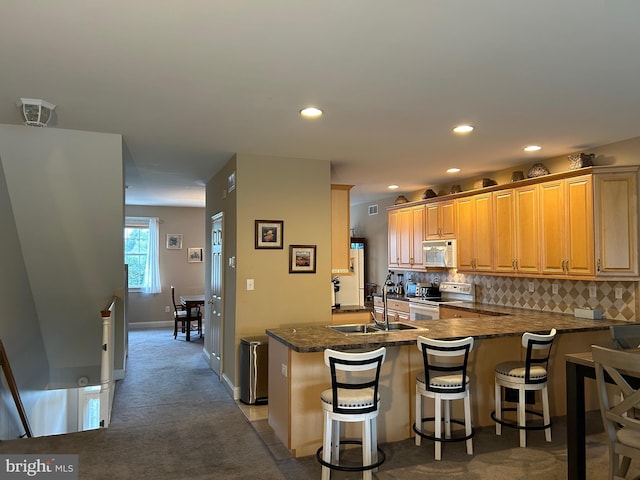 kitchen with decorative backsplash, carpet flooring, a sink, white appliances, and a peninsula