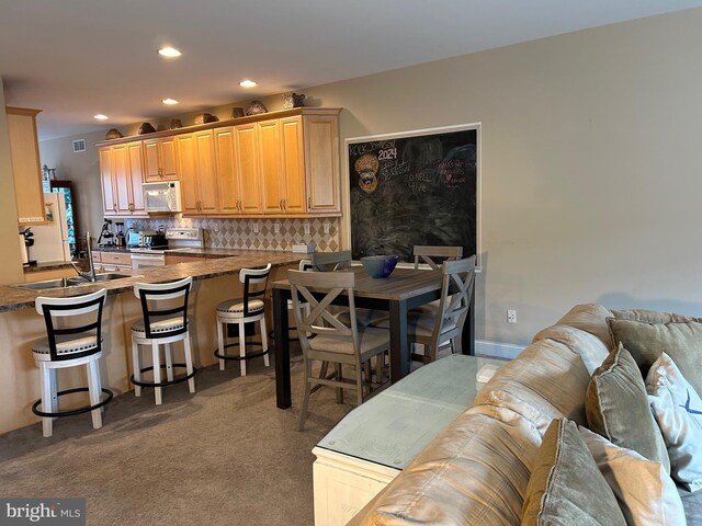 kitchen with carpet, decorative backsplash, a sink, white appliances, and a peninsula