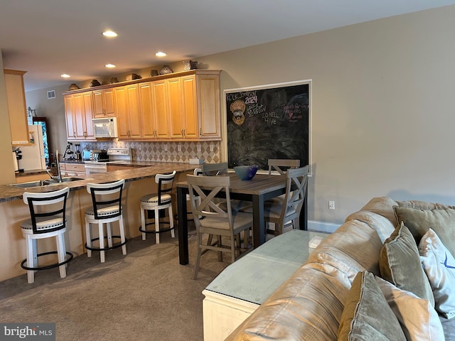 kitchen featuring white appliances, dark carpet, kitchen peninsula, backsplash, and a kitchen bar