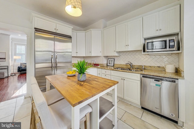 kitchen with built in appliances, sink, white cabinetry, light stone counters, and light wood-type flooring