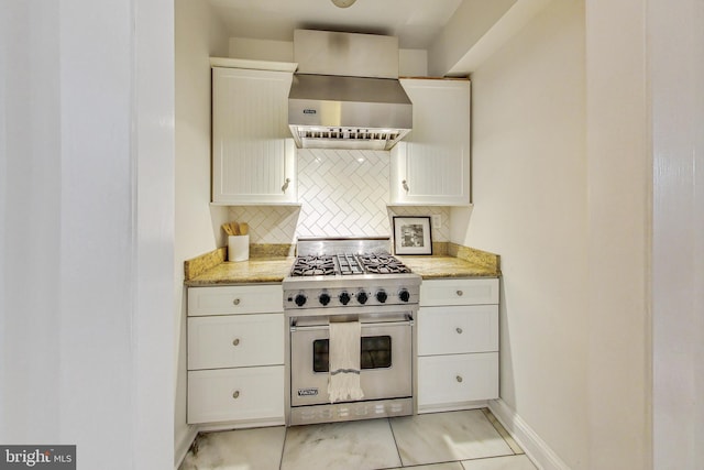 kitchen with light tile patterned floors, tasteful backsplash, premium stove, white cabinetry, and wall chimney range hood