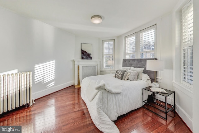 bedroom with dark wood-type flooring, radiator, and a fireplace