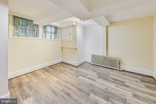 basement with radiator and light hardwood / wood-style flooring