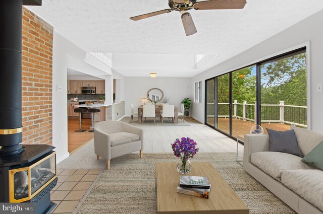 living room with a wood stove, ceiling fan, light wood-type flooring, and a textured ceiling