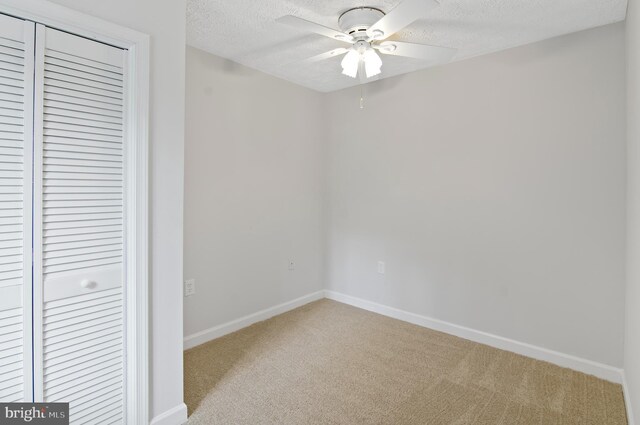 unfurnished bedroom featuring a textured ceiling, light colored carpet, ceiling fan, and a closet