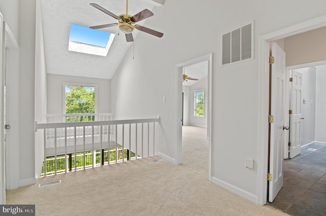 hallway featuring high vaulted ceiling, a skylight, a healthy amount of sunlight, and carpet