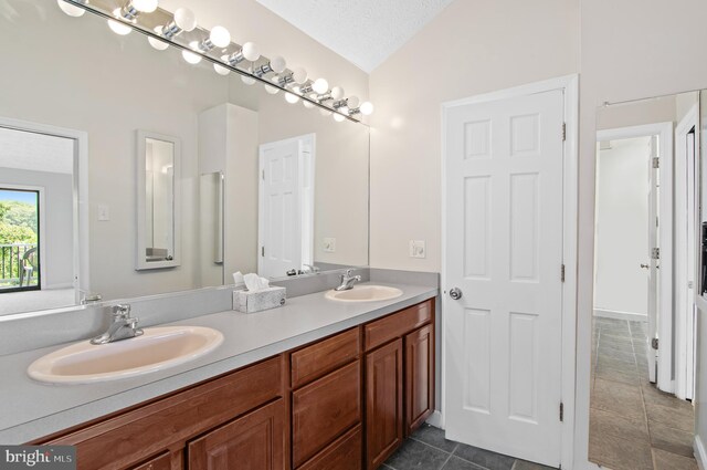 bathroom with a textured ceiling, vanity, vaulted ceiling, and tile patterned floors