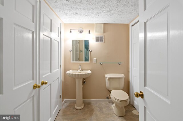 bathroom with a textured ceiling, toilet, and tile patterned floors