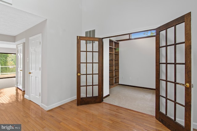 empty room with a healthy amount of sunlight, light wood-type flooring, and french doors