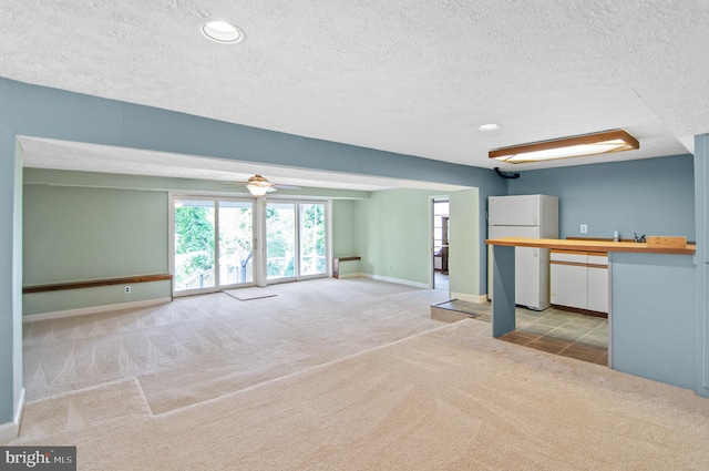 unfurnished living room with light carpet, a textured ceiling, and ceiling fan