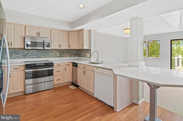 kitchen featuring light hardwood / wood-style flooring, kitchen peninsula, appliances with stainless steel finishes, and light brown cabinetry