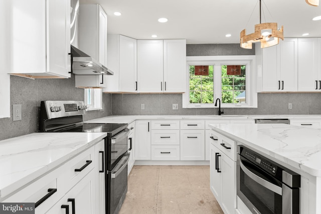 kitchen with wall chimney range hood, appliances with stainless steel finishes, white cabinetry, light stone countertops, and sink