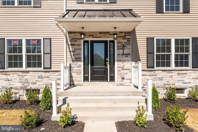 view of exterior entry featuring stone siding and a standing seam roof