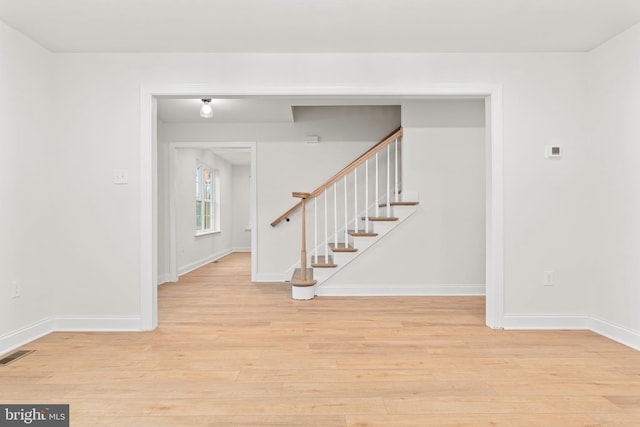 empty room with visible vents, baseboards, light wood-style floors, and stairway