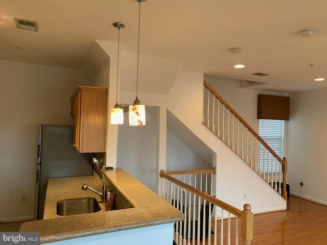 kitchen featuring sink, stainless steel refrigerator, decorative light fixtures, kitchen peninsula, and light wood-type flooring