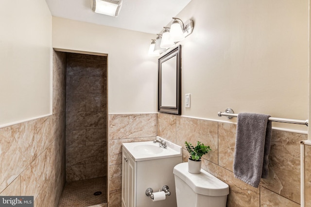 bathroom featuring vanity, toilet, a tile shower, and tile walls