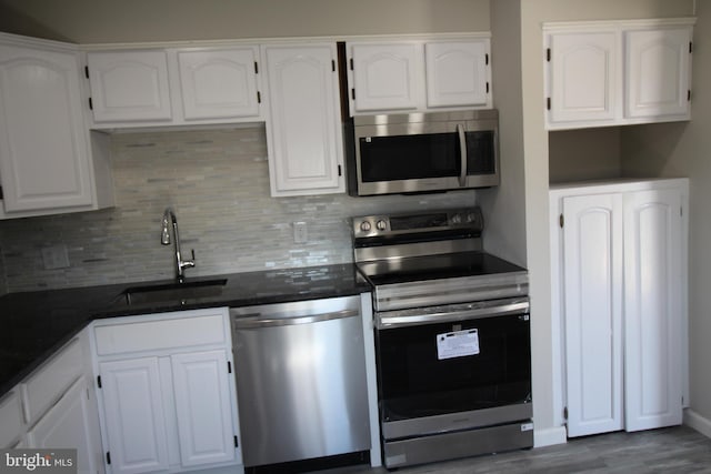 kitchen with a sink, stainless steel appliances, dark wood-type flooring, white cabinets, and tasteful backsplash