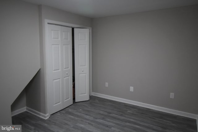 unfurnished bedroom with dark wood finished floors, a closet, and baseboards