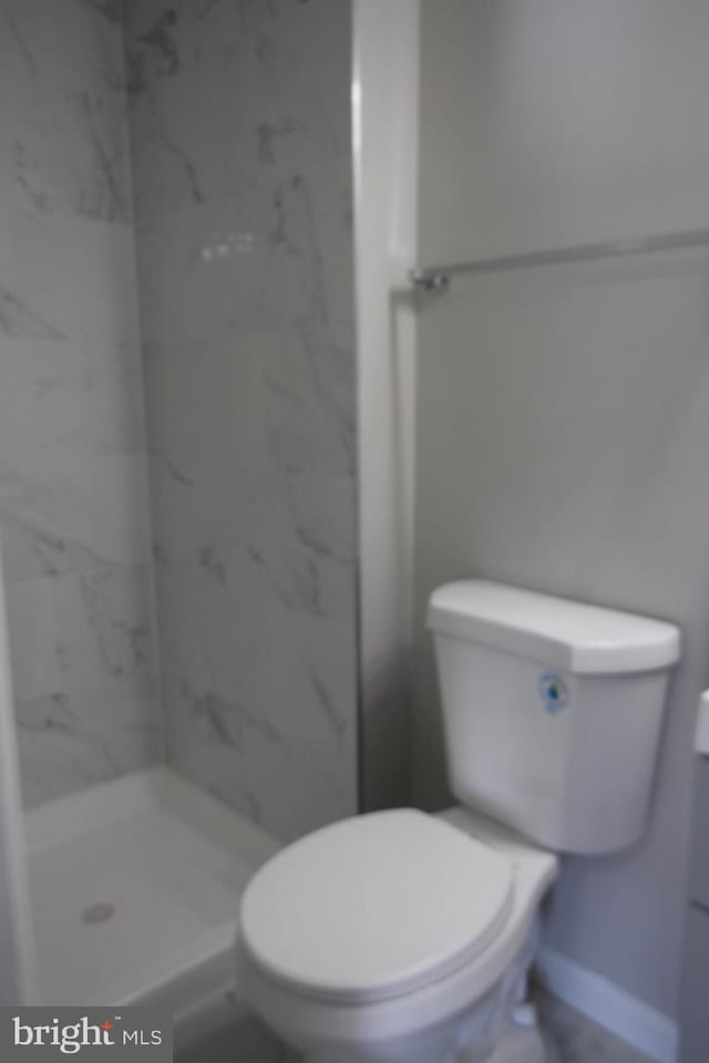 bathroom featuring a marble finish shower, toilet, and baseboards