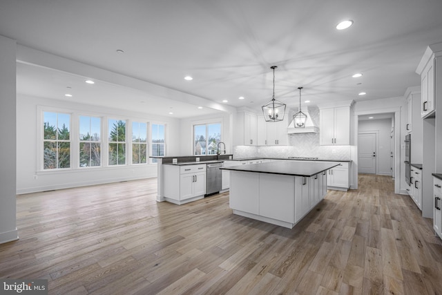 kitchen with white cabinets, a center island, appliances with stainless steel finishes, light hardwood / wood-style floors, and decorative backsplash