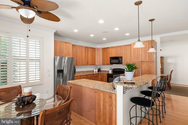 kitchen featuring light hardwood / wood-style flooring, a breakfast bar area, hanging light fixtures, ornamental molding, and black appliances