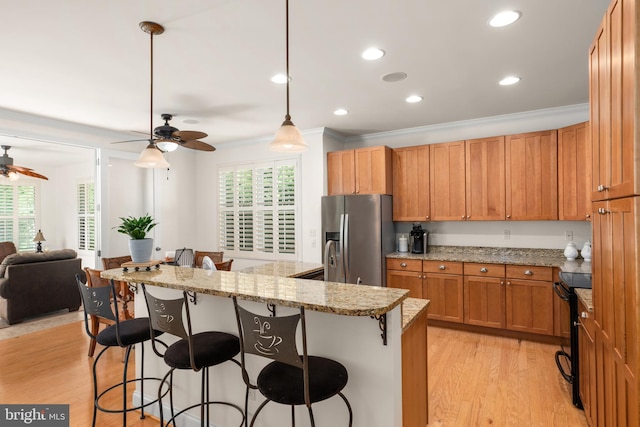 kitchen with light stone counters, hanging light fixtures, stainless steel fridge, a kitchen breakfast bar, and light hardwood / wood-style floors