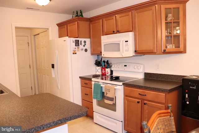 kitchen with visible vents, brown cabinets, dark countertops, white appliances, and glass insert cabinets