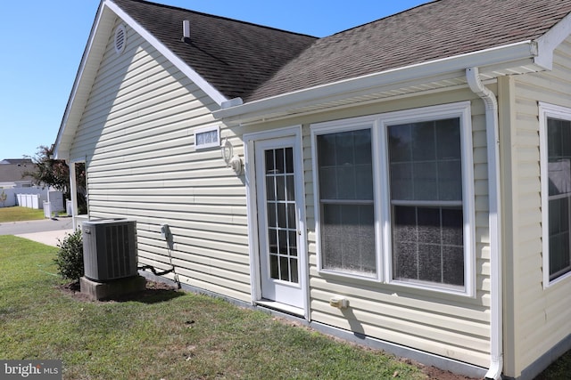 view of side of property featuring cooling unit, a shingled roof, and a yard