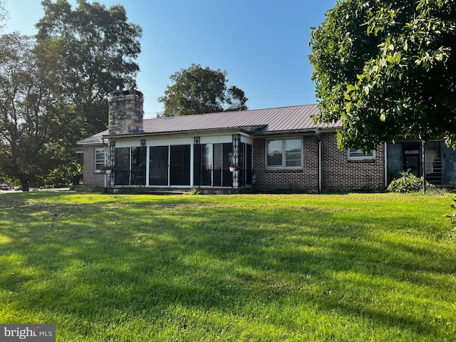 back of property featuring brick siding, a chimney, metal roof, a yard, and a sunroom