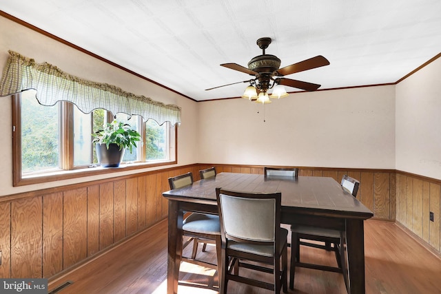 dining area with hardwood / wood-style floors, ceiling fan, wooden walls, and ornamental molding