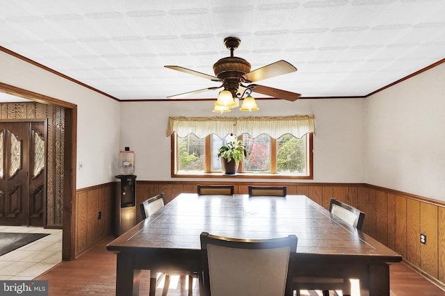 dining space with crown molding, dark wood-type flooring, ceiling fan, and wooden walls