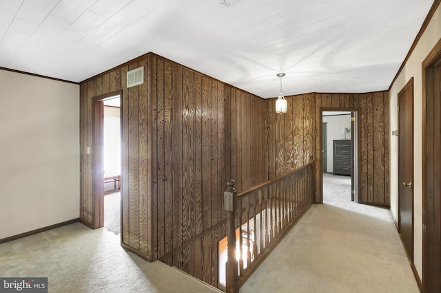 hall with light colored carpet, wooden walls, and ornamental molding